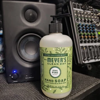 Mrs. Meyer’s Clean Day Iowa Pine hand soap bottle on a studio desk with a speaker and audio equipment in the background.